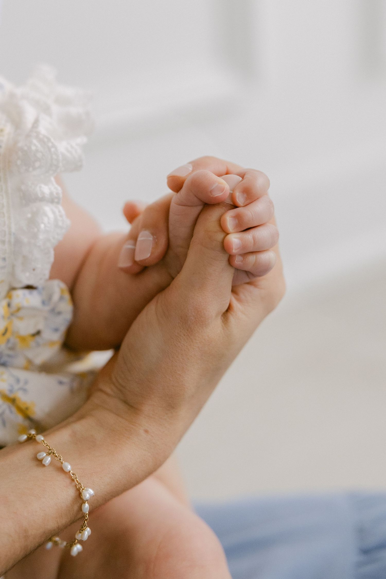A delicate pearl bracelet adorns a wrist as hands clasp together in a gentle, intimate moment.