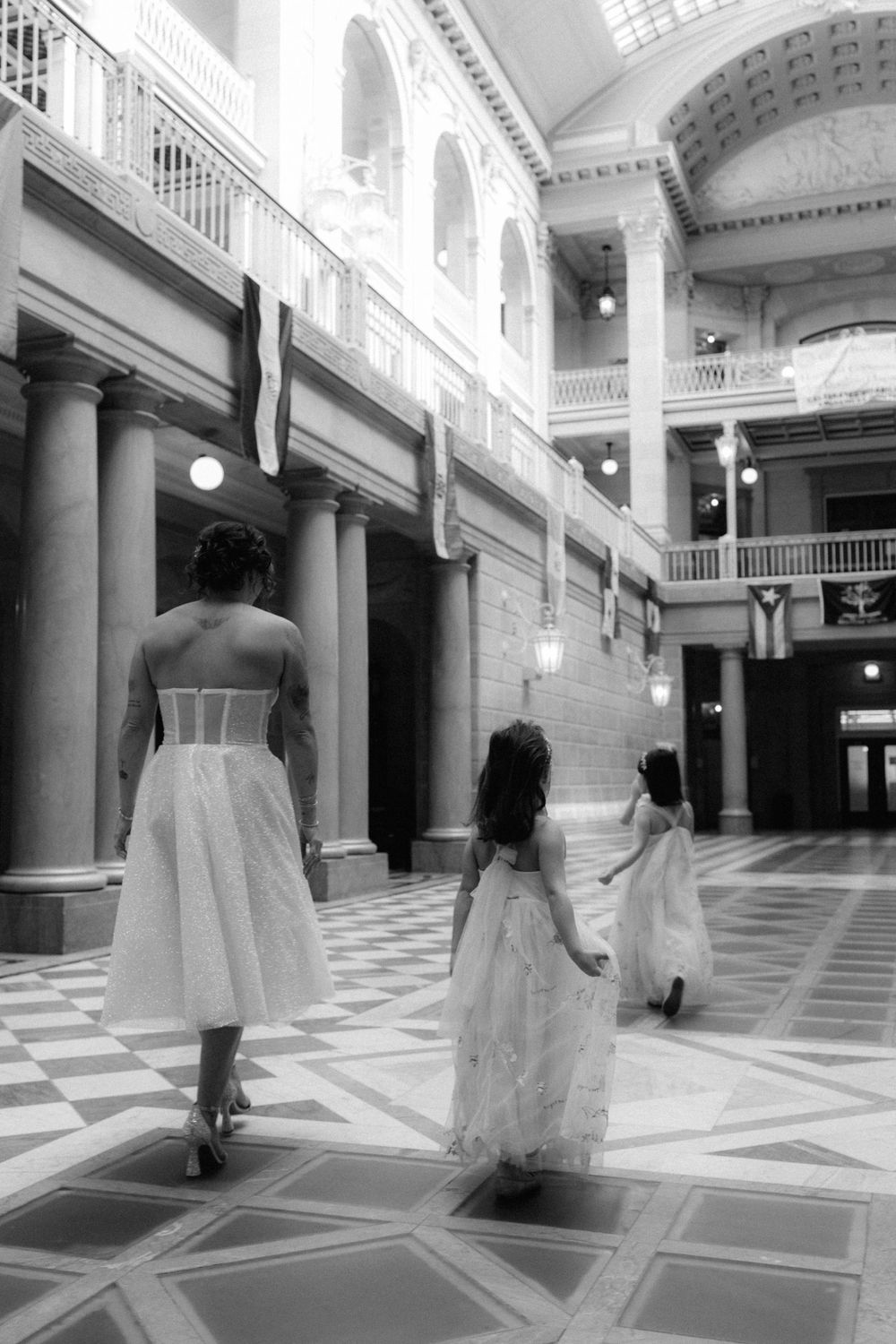 Black and white photo of a bride and two flower girls walking through an elegant columned hall.
