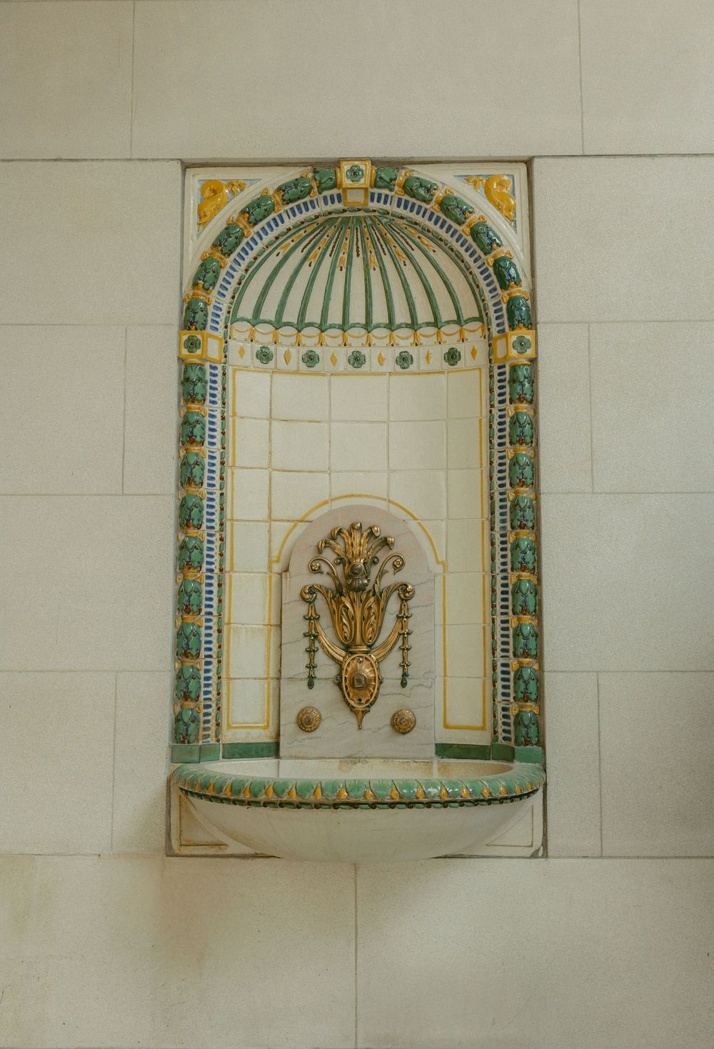 Ornate decorative wall niche with gold floral motif, green and yellow mosaic tiles, and arched dome design.