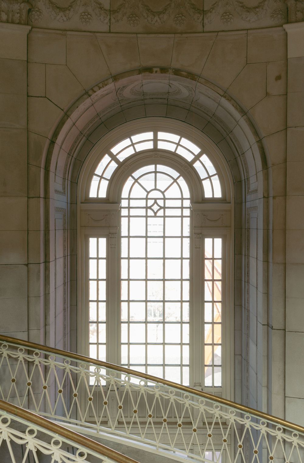 Elegant arched window with ornate stone surrounds and decorative iron railing on a grand staircase in a classical building.