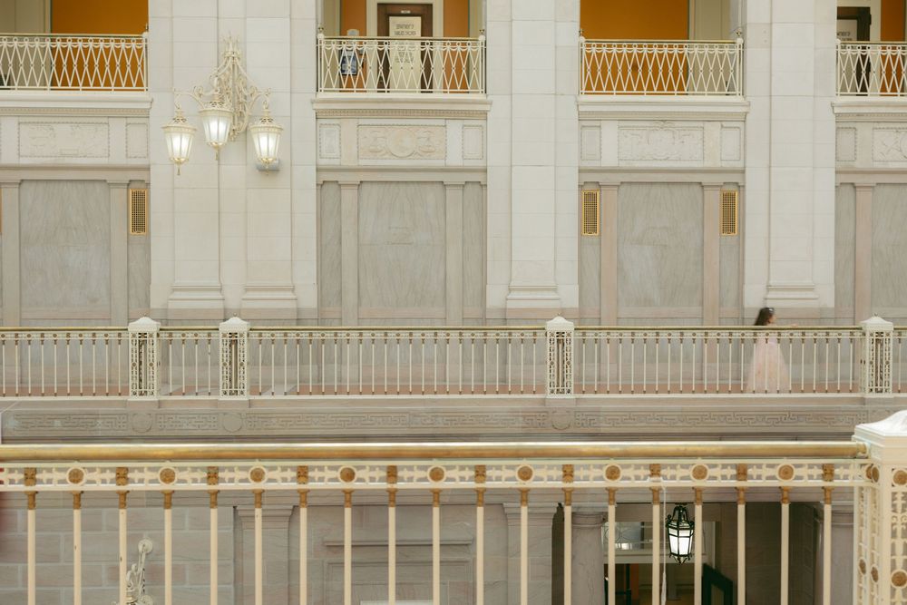 Elegant grand interior with white marble columns, ornate gold railings, and a chandelier in a classical architectural space.