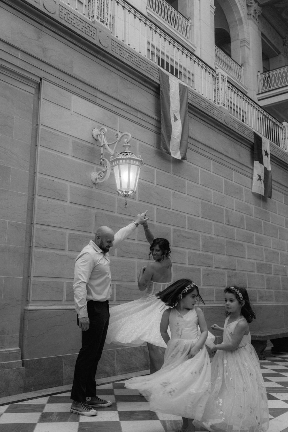 Black and white photo of a couple dancing with two flower girls in white dresses at a wedding venue.