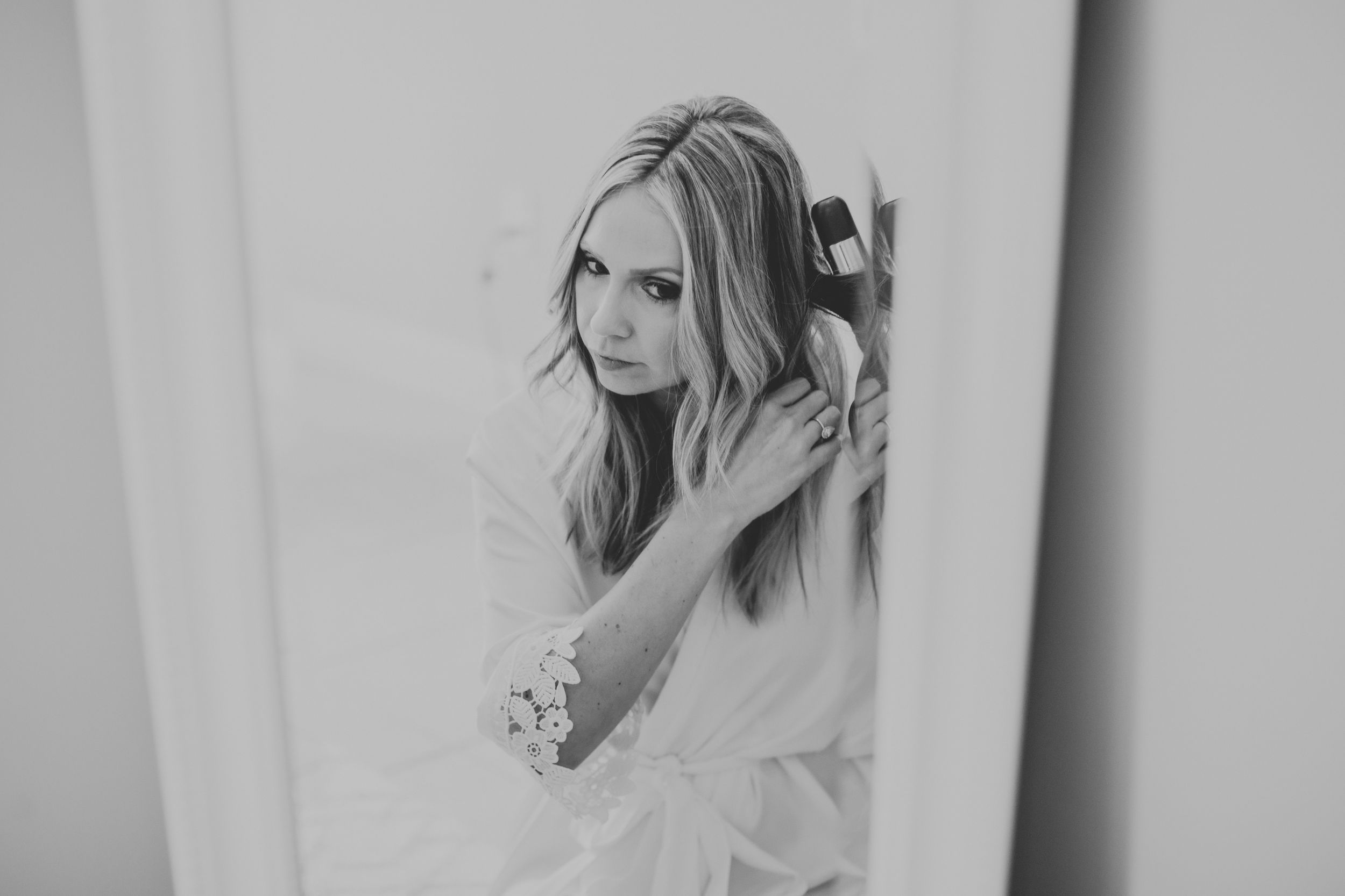Black and white photo of a blonde woman in a white robe brushing her long hair while looking over her shoulder.