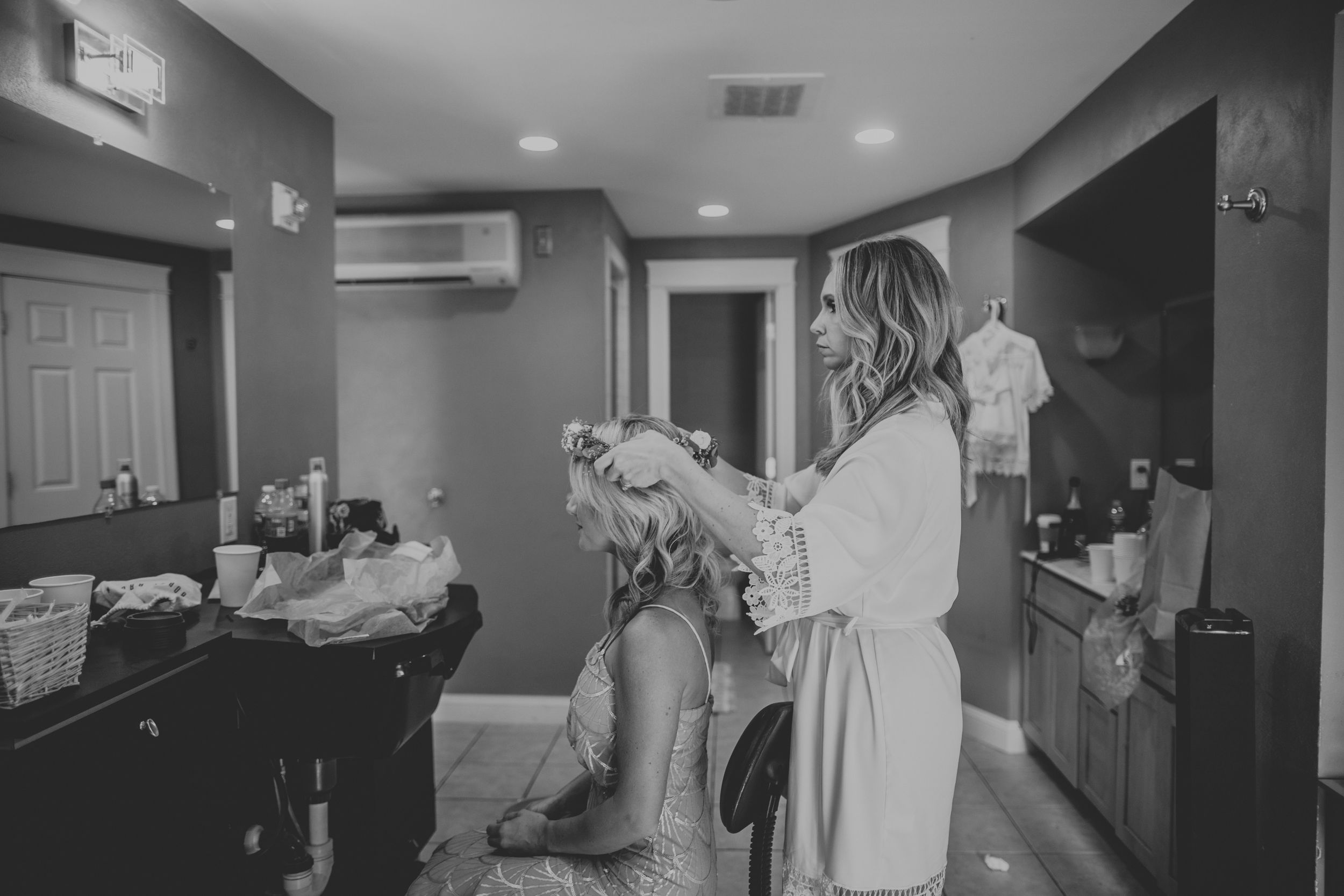 Black and white photo of a bride having her hair styled by a hairdresser in a bridal suite.