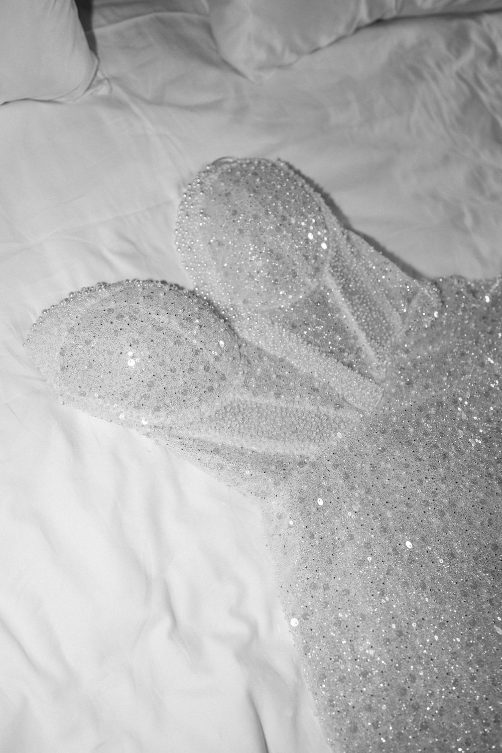 Black and white photo of a sparkling sequined dress laid flat on white rumpled bed sheets.