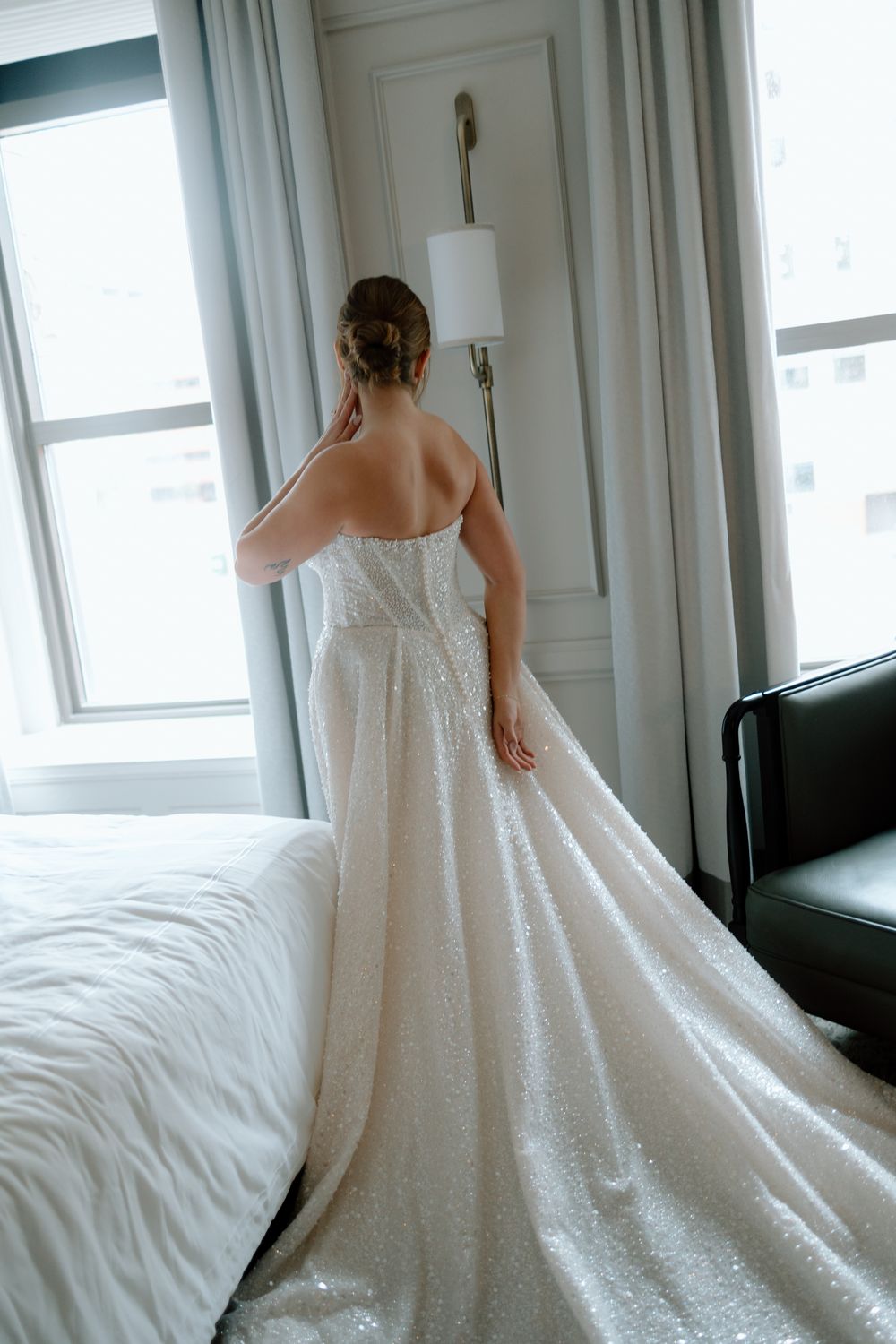 Editorial bride gets ready at the Pfister hotel with a long train stands by a window in Milwaukee