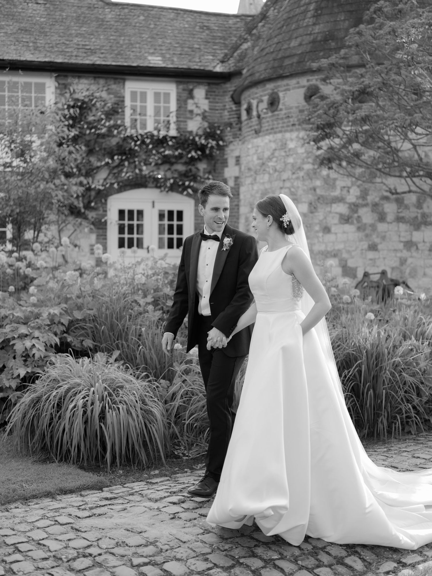 A couple in wedding attire share a joyful moment outdoors, with the bride in a lace dress and groom in light gray suit.
