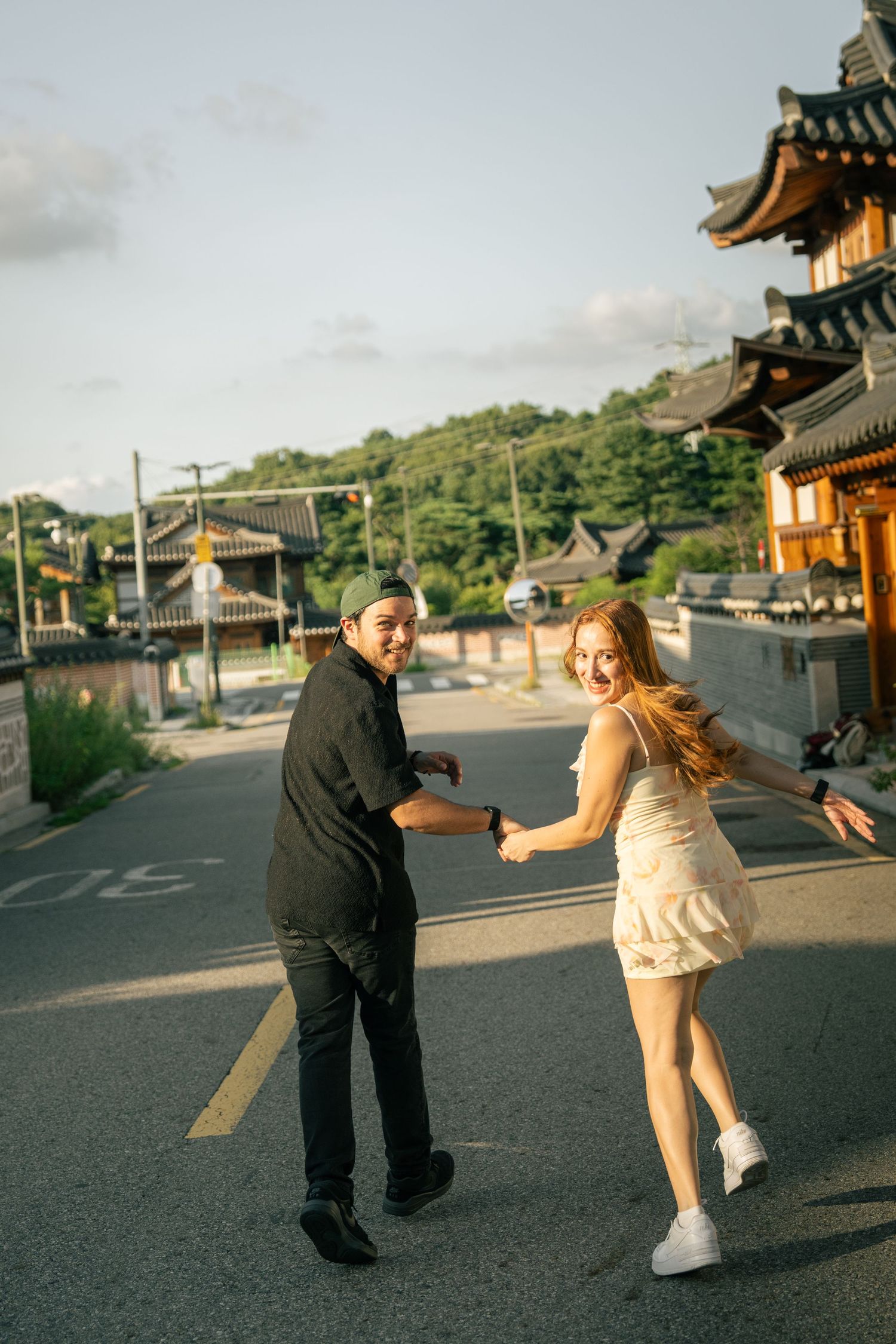 A couple playfully poses in a sequence of photos on a street with traditional Asian architecture in the background.