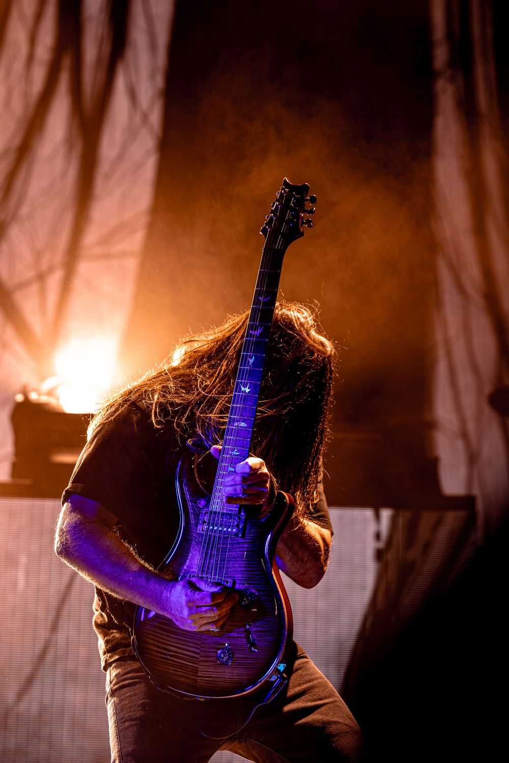 Electric guitar player silhouetted against warm orange lighting with dramatic blue glow on the instrument.