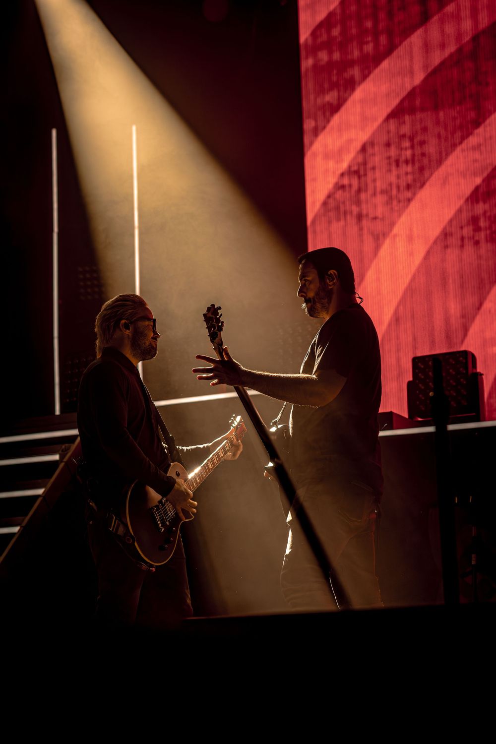 Silhouetted musicians perform on stage with dramatic red lighting and beams creating atmospheric shadows.