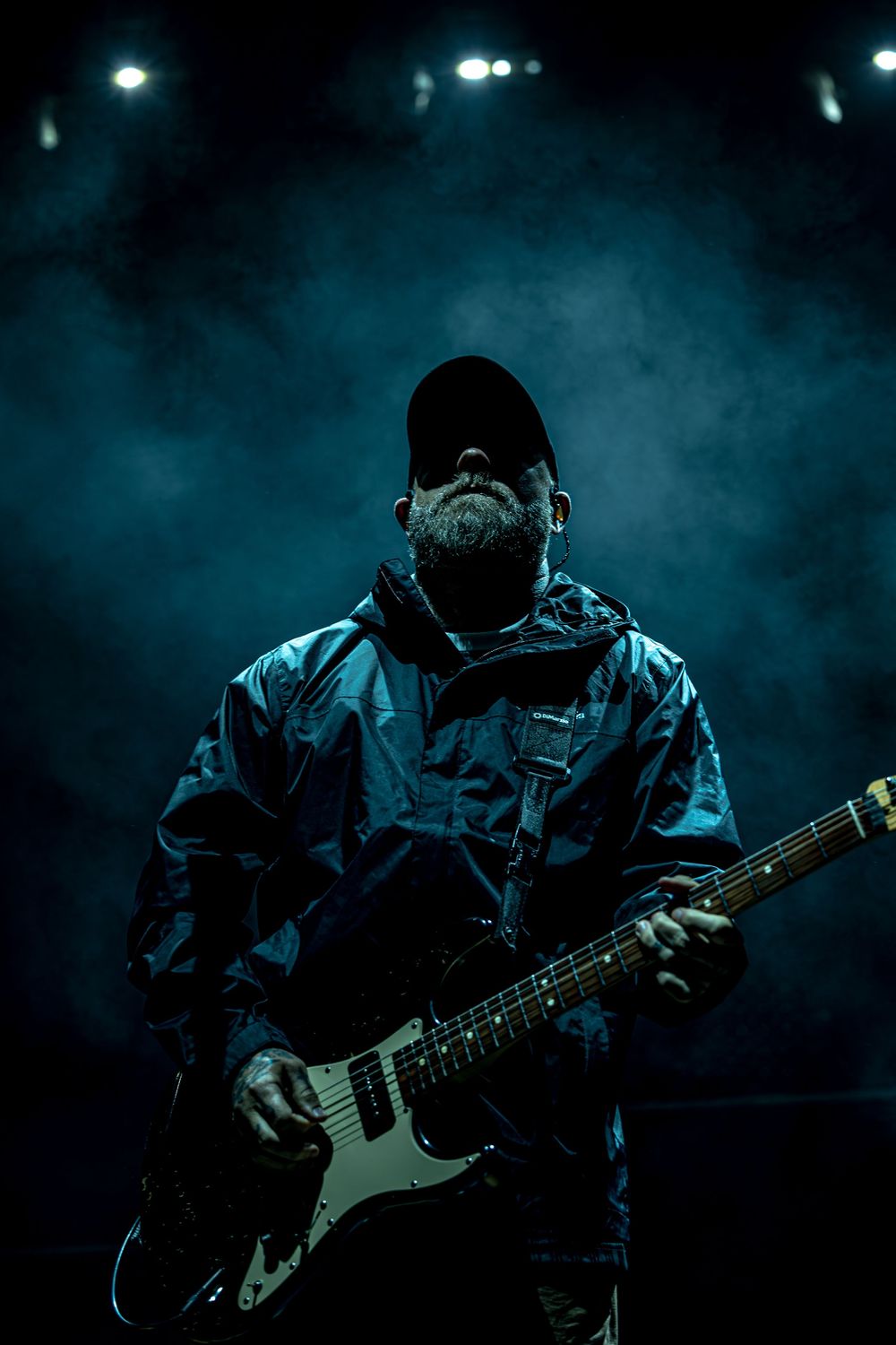 A guitarist performs on stage in dramatic blue lighting with smoke effects creating a moody atmosphere.