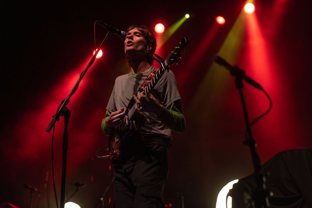 Musicians perform on stage under dramatic red lighting during a live concert performance.