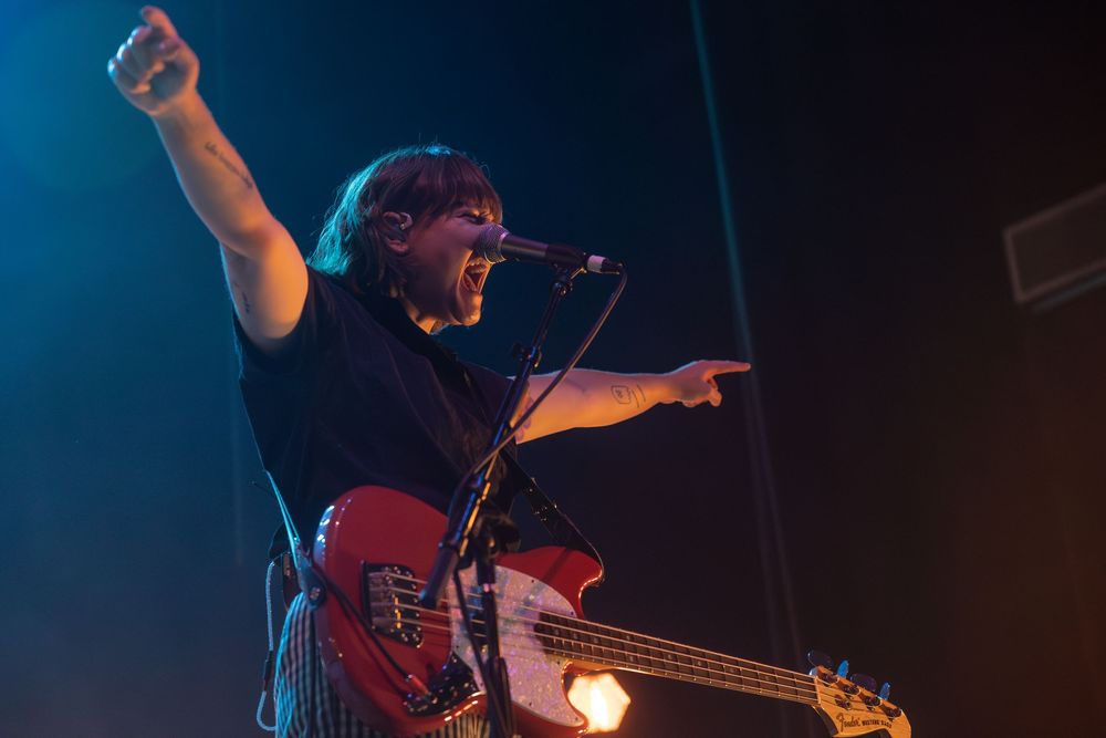 Musician performs energetically on stage with a bass guitar under blue lighting.