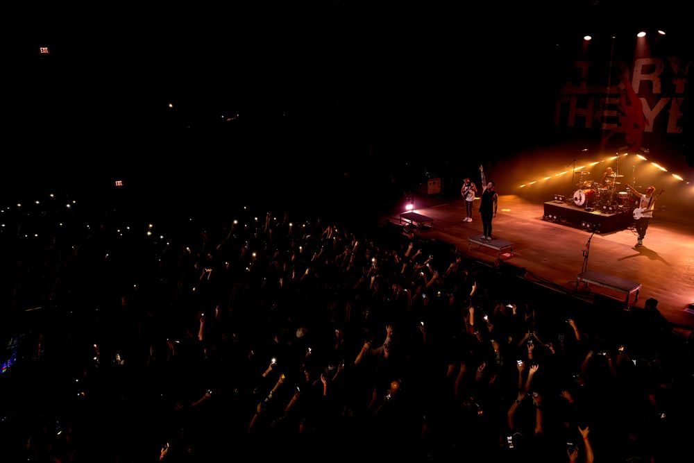 Aerial view of a dark outdoor concert venue at night with scattered lights illuminating the crowd and stage area.