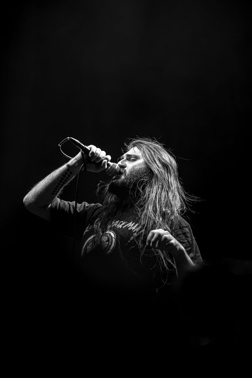 Dramatic black and white silhouettes of a performer singing on stage with long hair in motion against dark background.