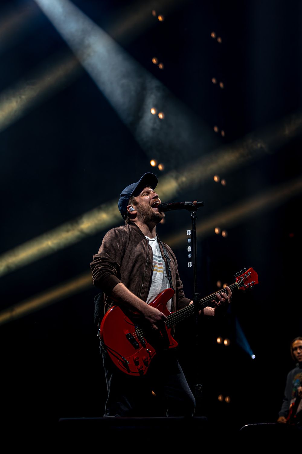 Musician performs passionately on stage with red guitar under dramatic concert lighting and spotlights.