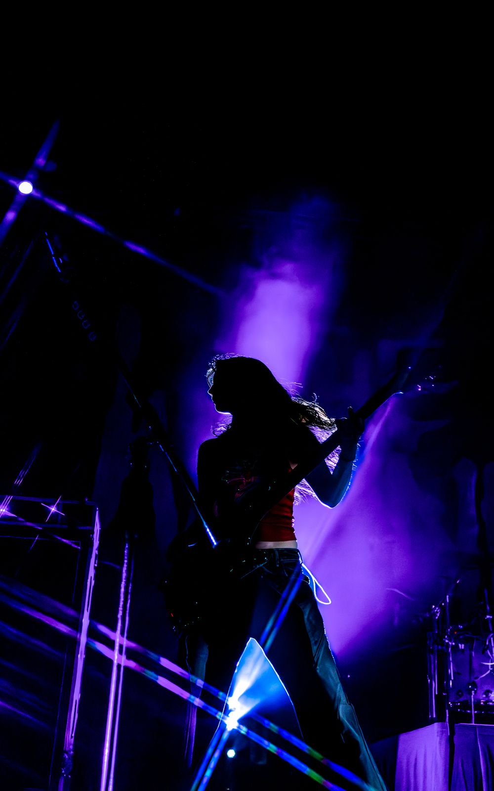 Silhouetted performers on a dark stage illuminated by dramatic purple and blue lighting effects during a concert.