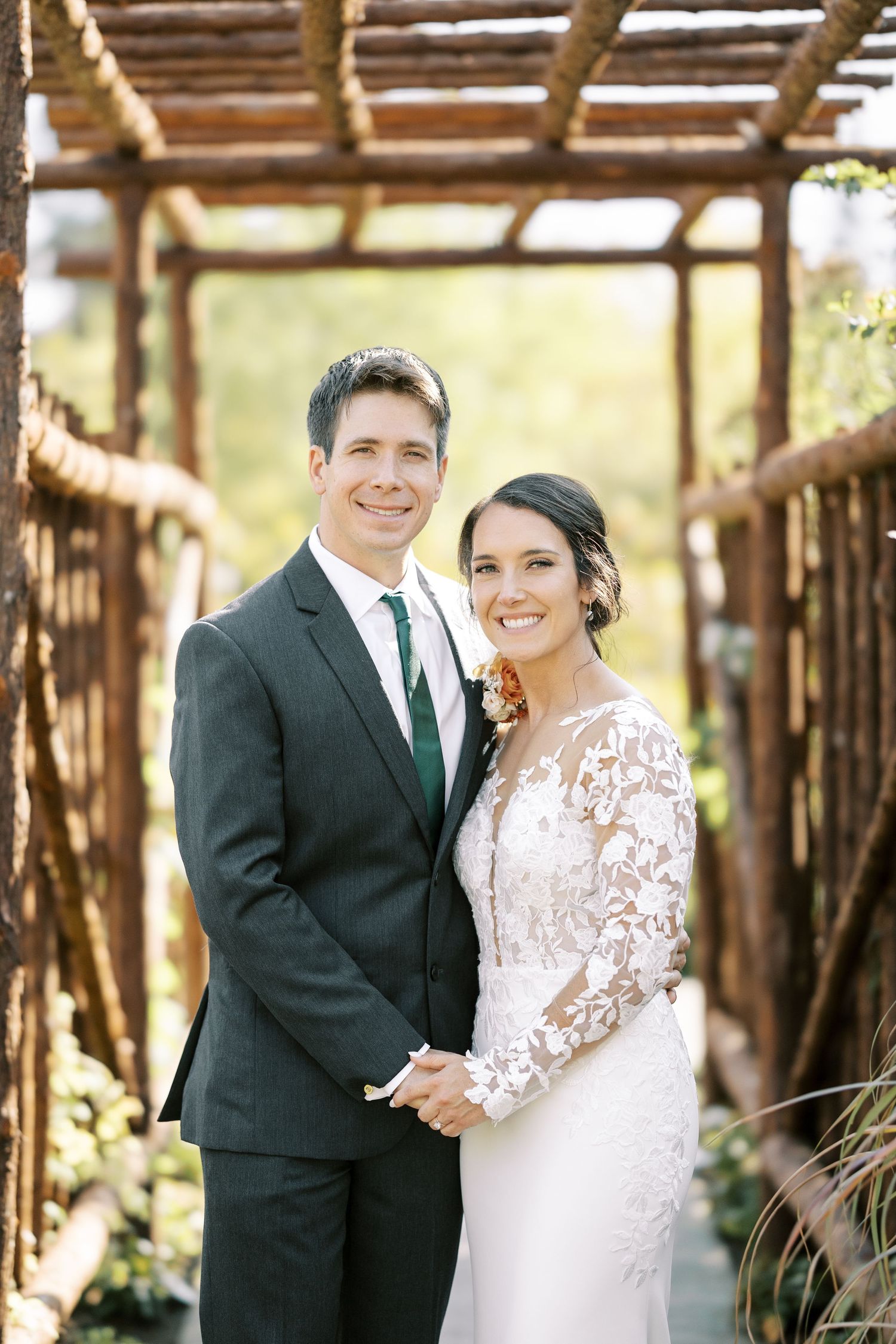 A couple in wedding attire shares joyful moments under a rustic wooden pergola on their special day.