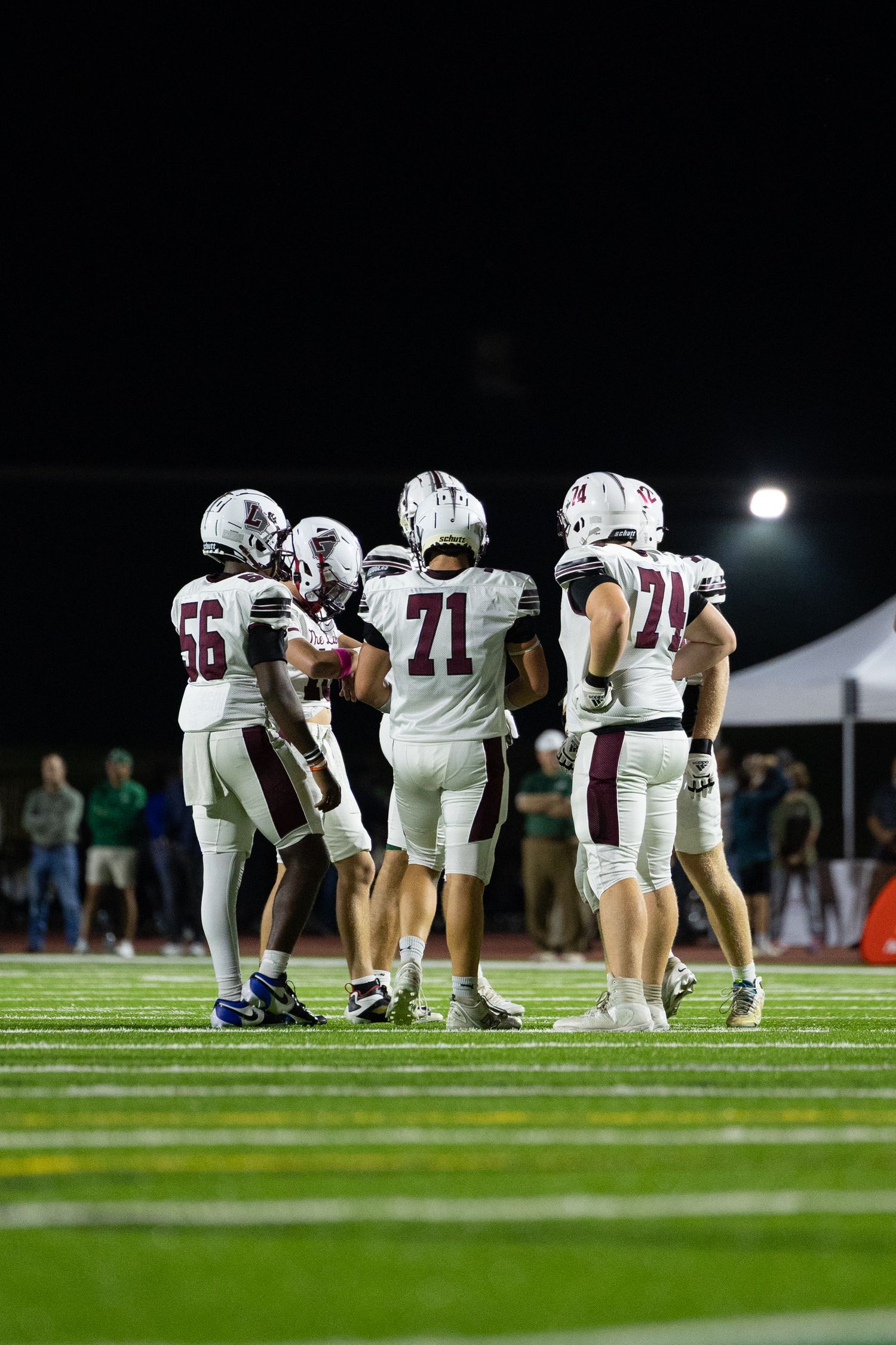 Football players line up in formation during a nighttime game on an illuminated field.