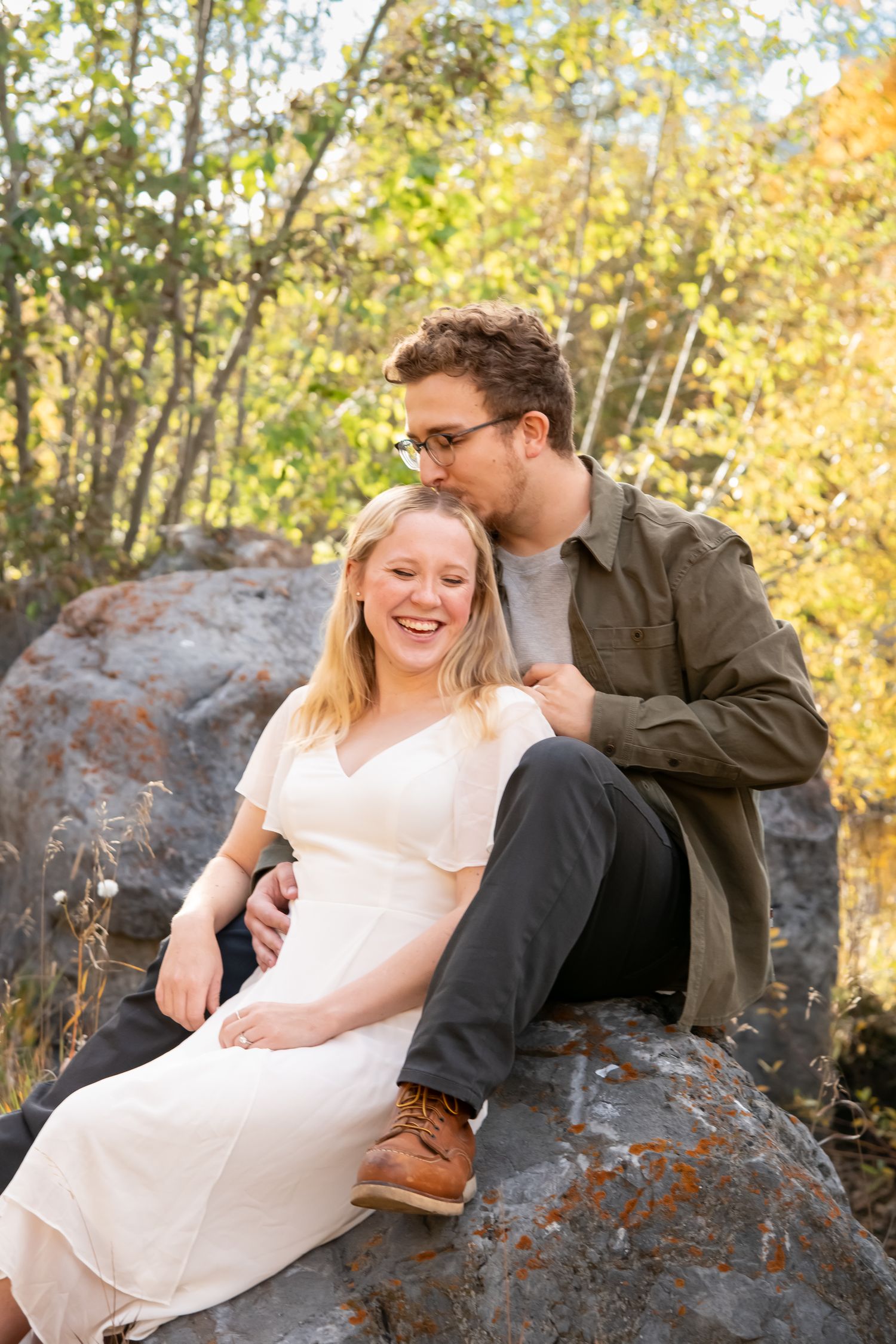 Candid photo of couple laughing while sitting on a rock with soft fall colors behind them during a fall engagement session in Vail Colorado