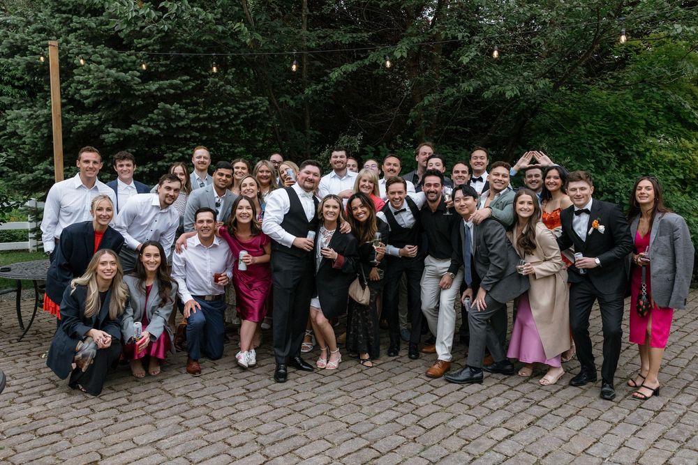 Large group of wedding guests gathered outdoors for a panoramic photo at a garden celebration.