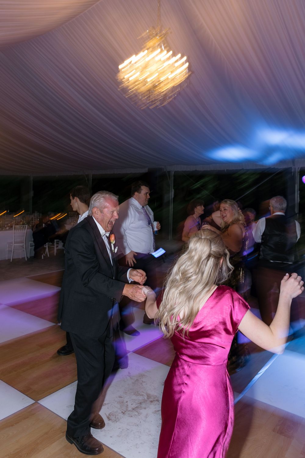 Couples dancing together under decorative lighting at an elegant wedding reception in a draped tent venue.
