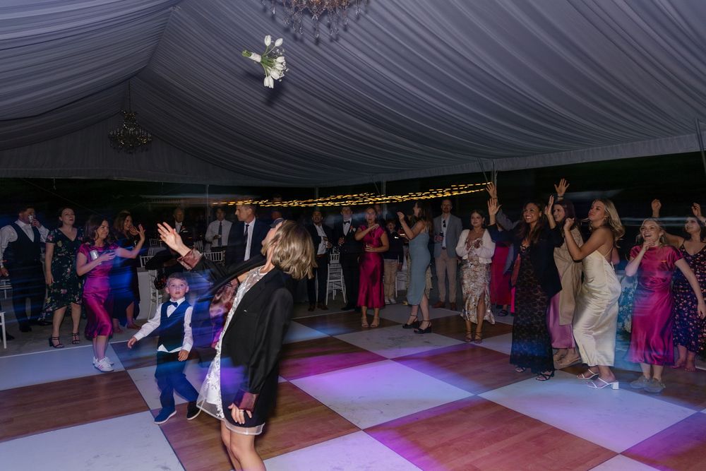 People dancing together on a dance floor under a white tent during an outdoor evening celebration.