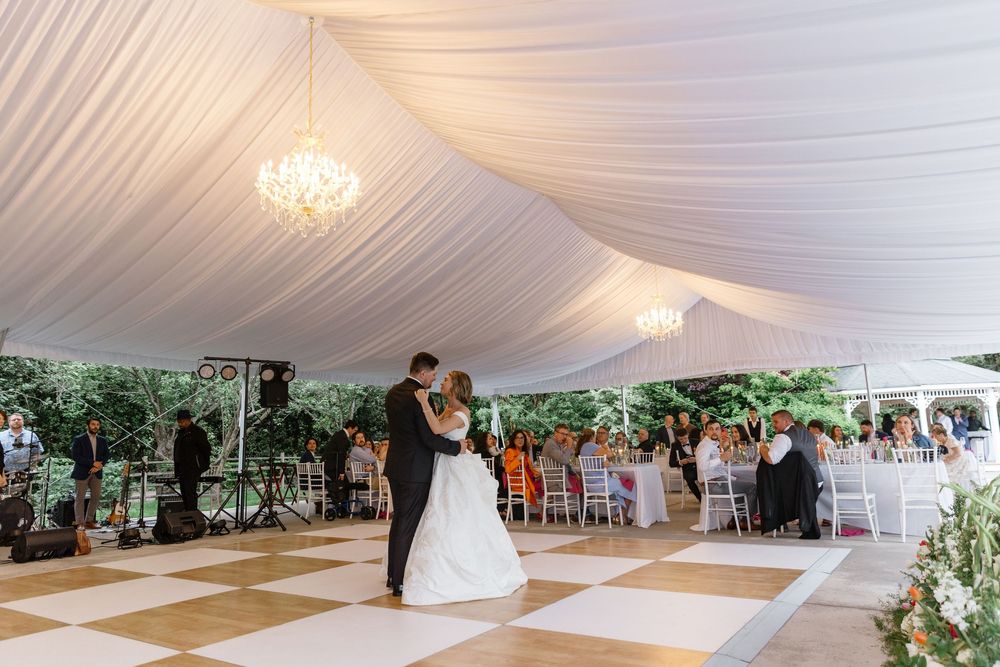 A white draped tent ceiling with elegant chandeliers creates a romantic atmosphere for an indoor wedding reception.