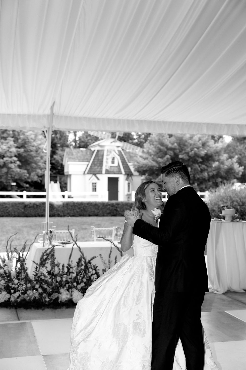 A couple in formal wedding attire dances together in a sequence of four black and white photos under a white tent.