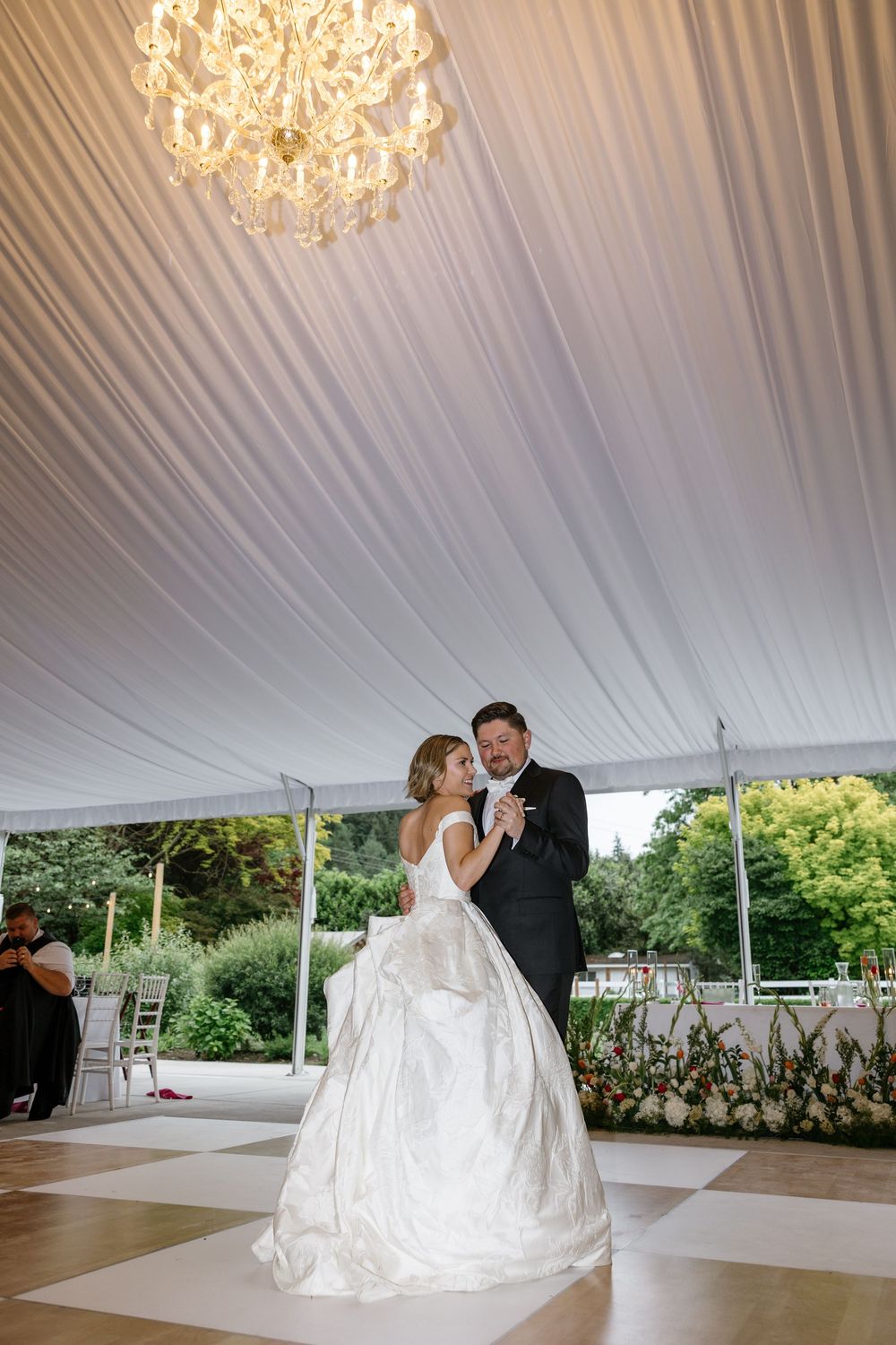 A couple shares their first dance under elegant crystal chandeliers in a white tent reception venue.