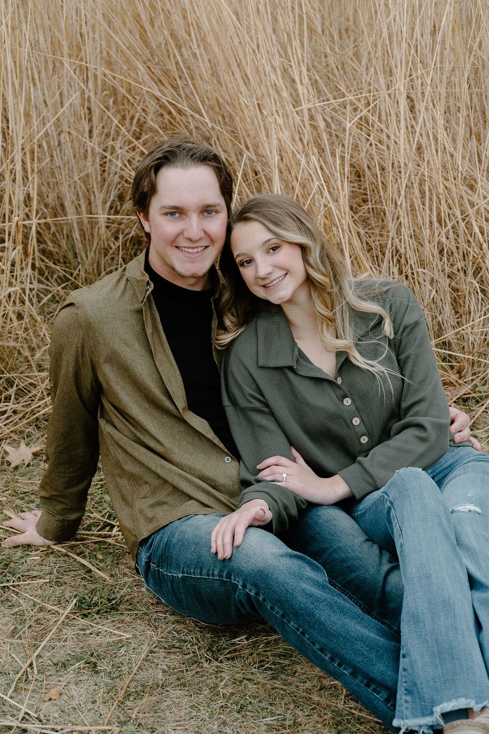 A couple sits together in tall golden grass wearing casual clothing in a series of candid outdoor portraits.