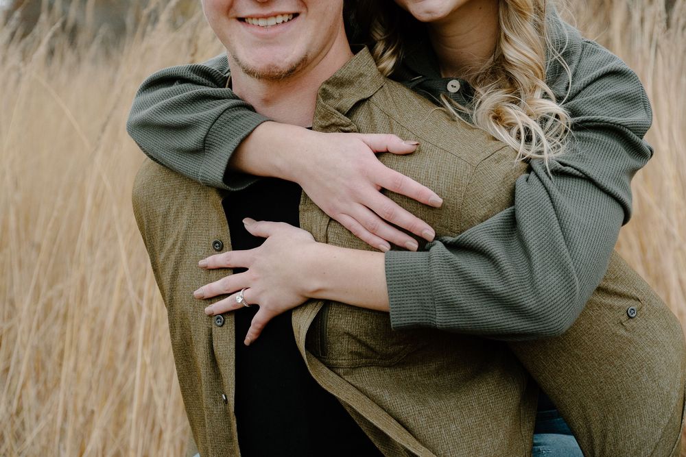 Close up of a couple embracing in tall grass wearing matching olive green shirts.