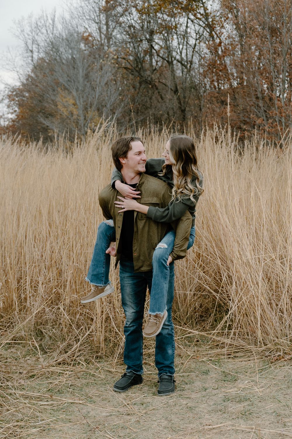 A couple shares a playful moment in a field of tall grass on an autumn day.