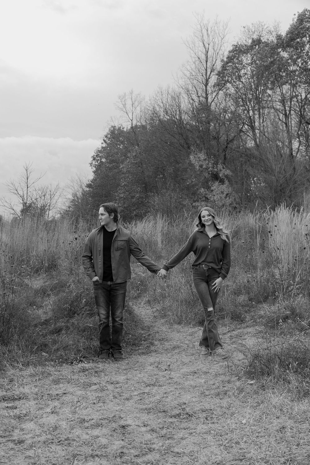 A black and white photo series shows two people playfully interacting on a grassy hillside in nature.