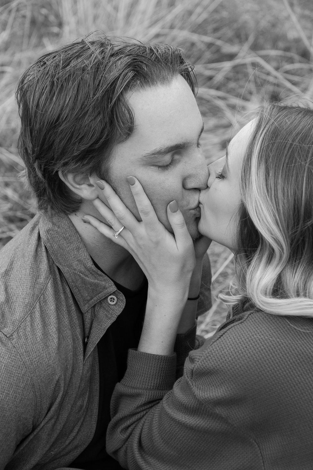 A romantic black and white photograph of a couple sharing a tender kiss in tall grass.