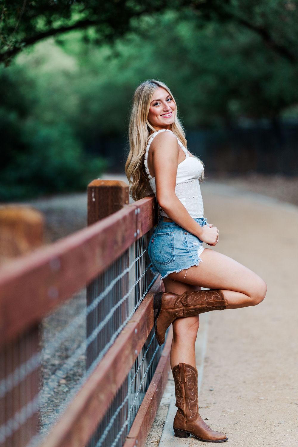Casual outdoor photoshoot featuring denim shorts and brown cowboy boots against rustic bridge railing.