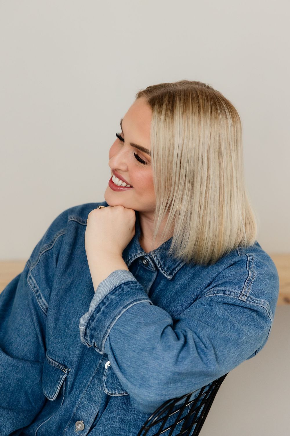 Candid portrait showing joyful expression while wearing denim jacket against light background.