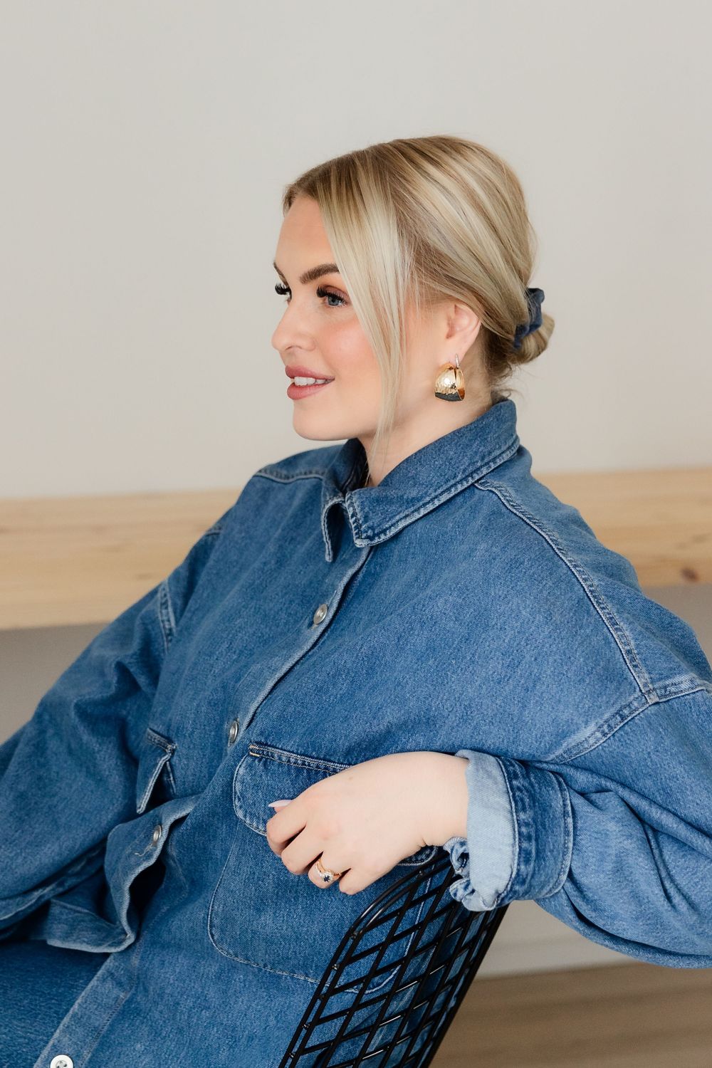 Side profile portrait showing elegant pose in oversized denim jacket with hair in low bun.