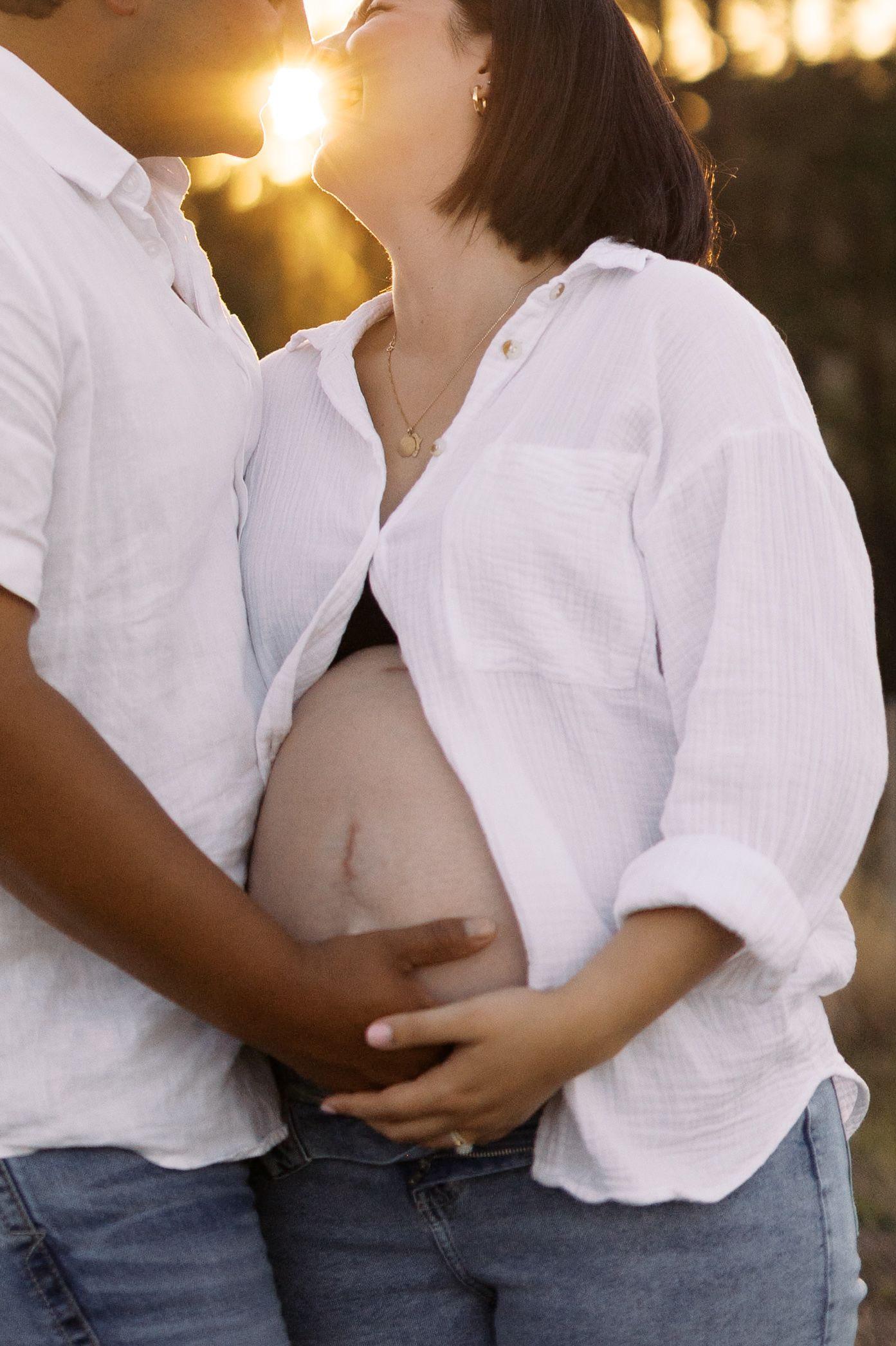 Intimate couple's photoshoot in white shirts against warm sunset lighting.