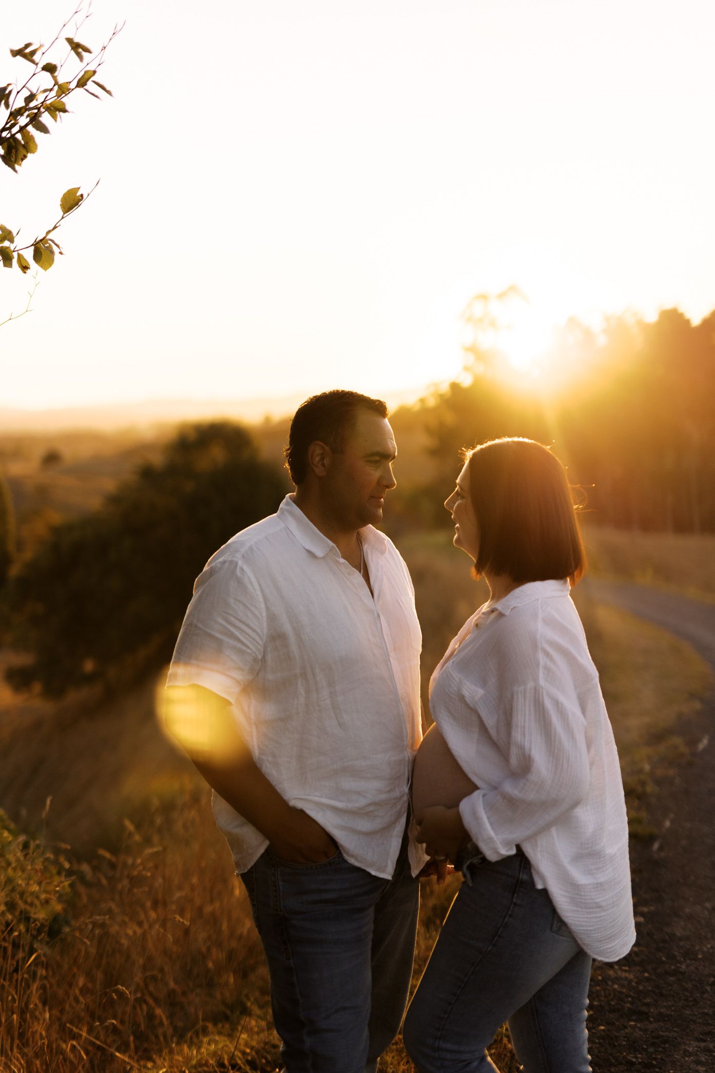 Couple sharing tender moments in matching white outfits during sunset in a field.