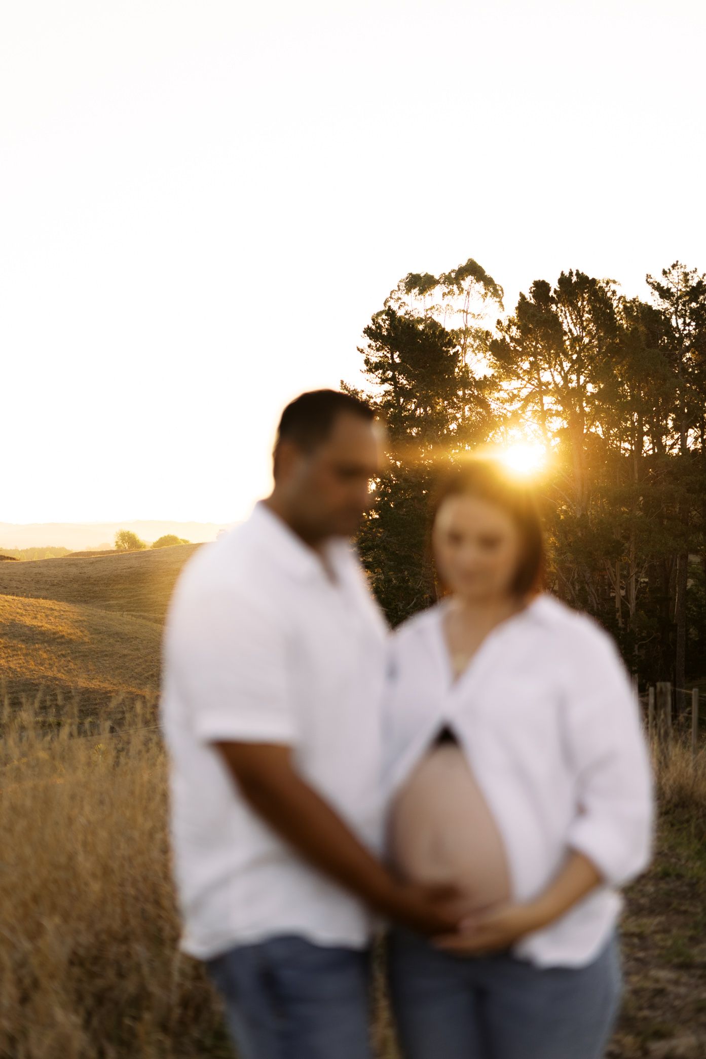 Two people in white tops and jeans embrace in a field during golden hour.