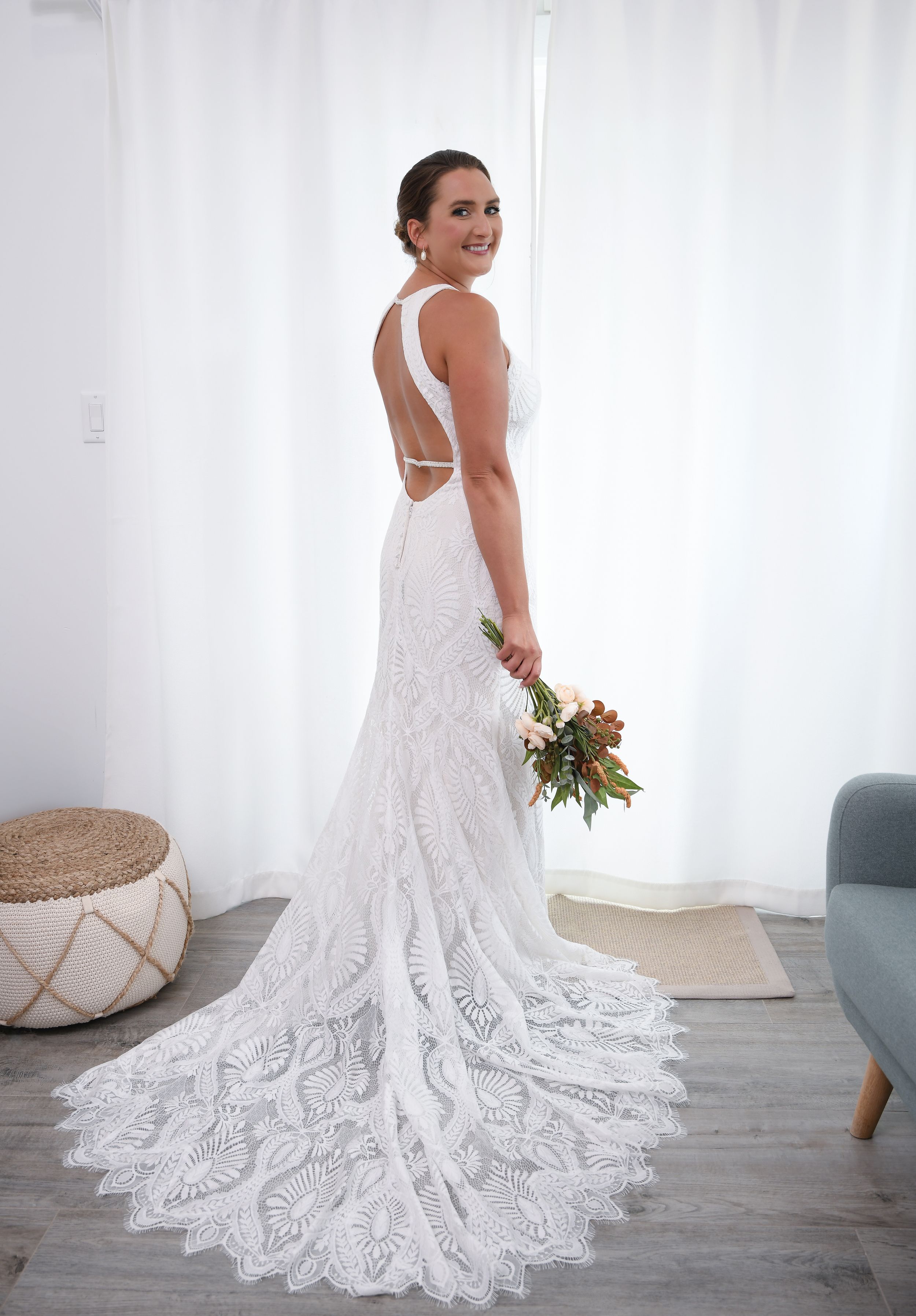A bride in a flowing lace wedding gown with a dramatic train poses in a bright white studio setting.