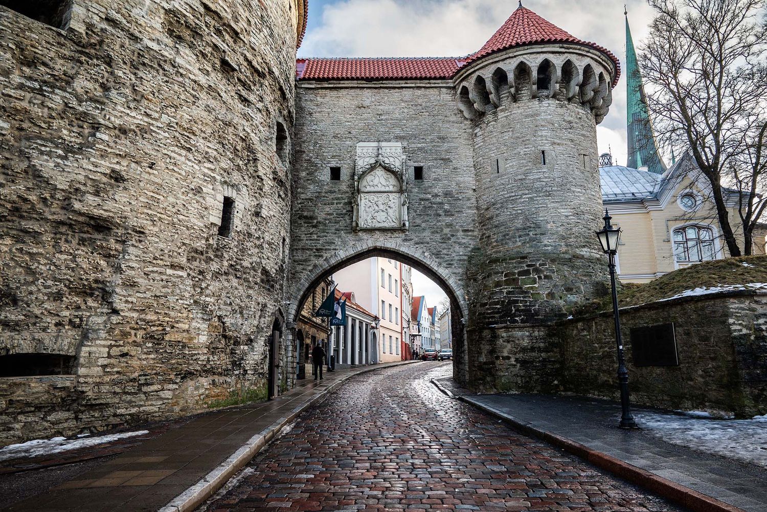 Medieval stone archway gate with turret leads to cobblestone street in historic Tallinn, Estonia on winter day.