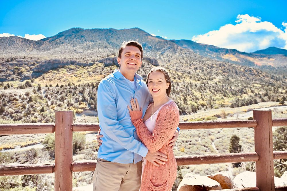 Smiling engaged couple posing together at a mountain overlook on a bright sunny day.
