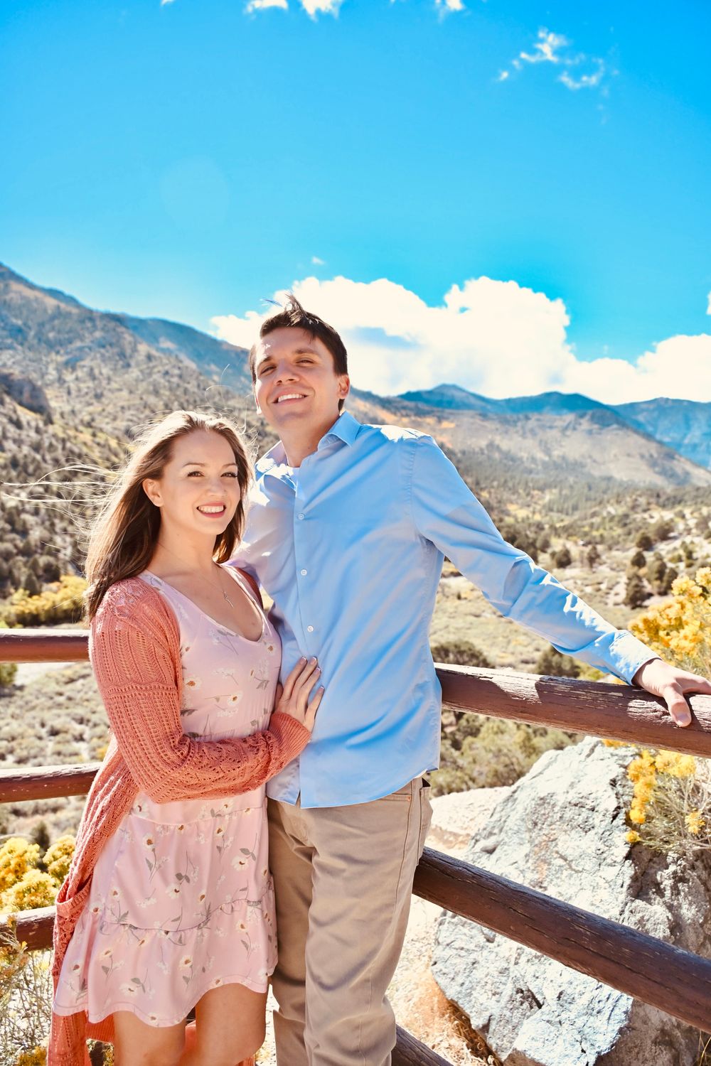 Cheerful couple standing together on a wooden railed mountain overlook enjoying the scenic view.