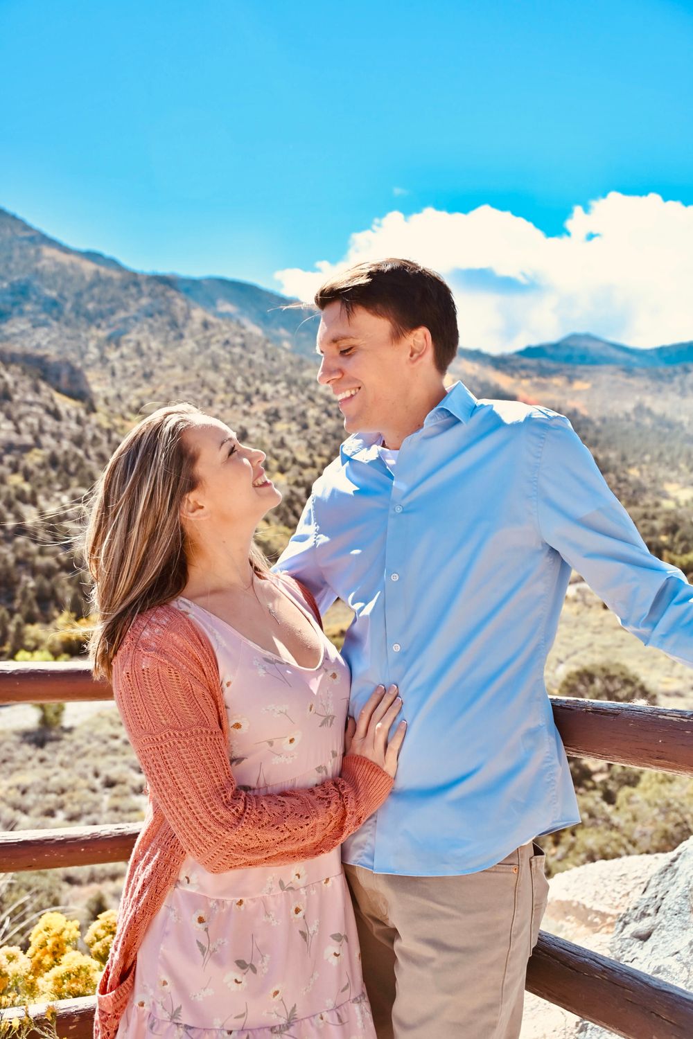 Couple gazing lovingly at each other on a mountain overlook, woman in pink dress, man in blue shirt.