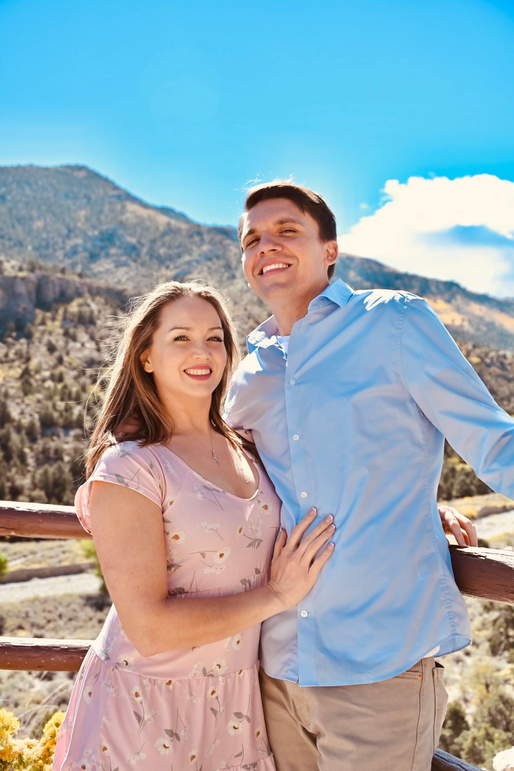 Happy couple embracing and smiling at camera on scenic mountain overlook on a sunny day.