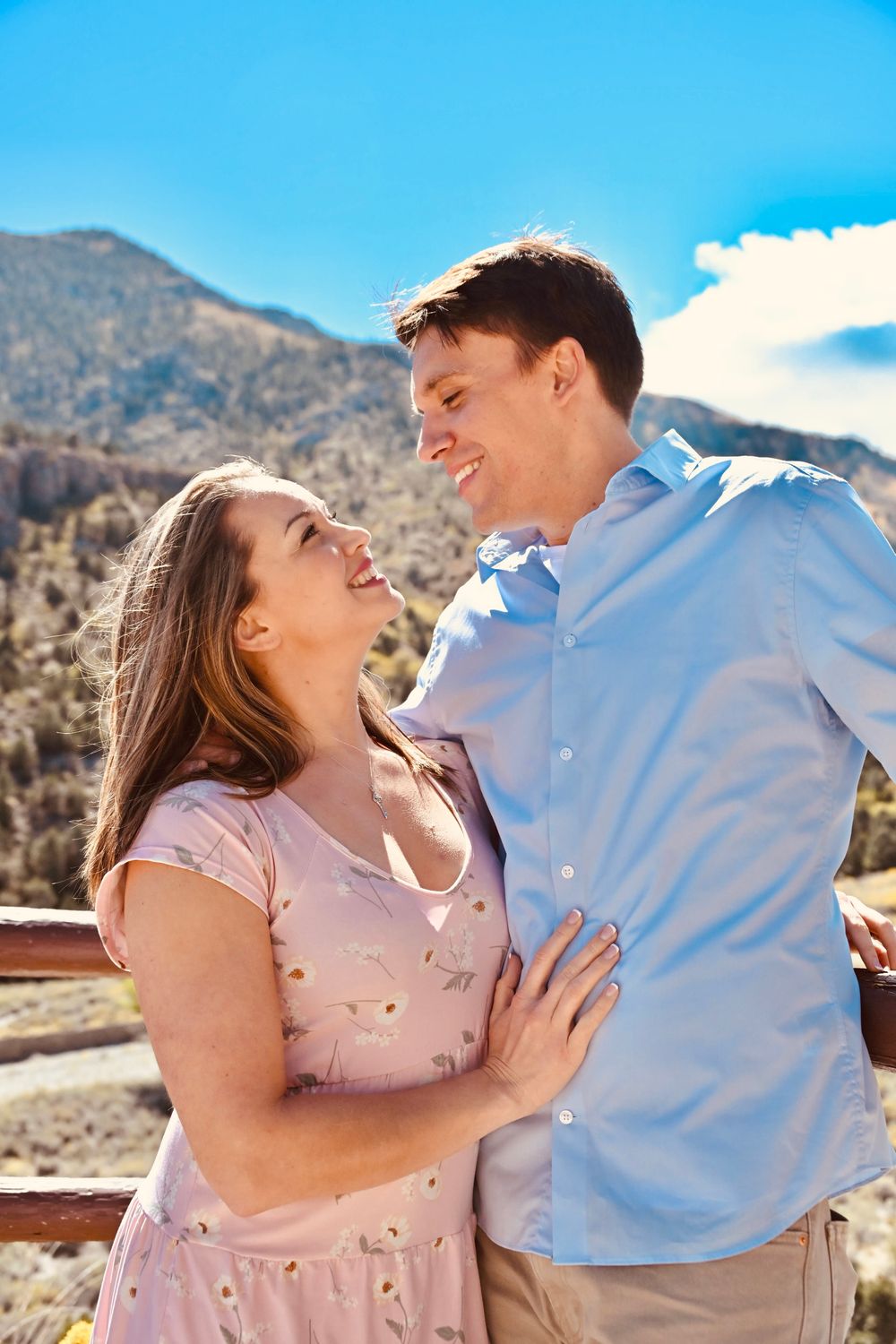 Romantic couple sharing a joyful moment together on a rustic wooden railing with mountain backdrop.