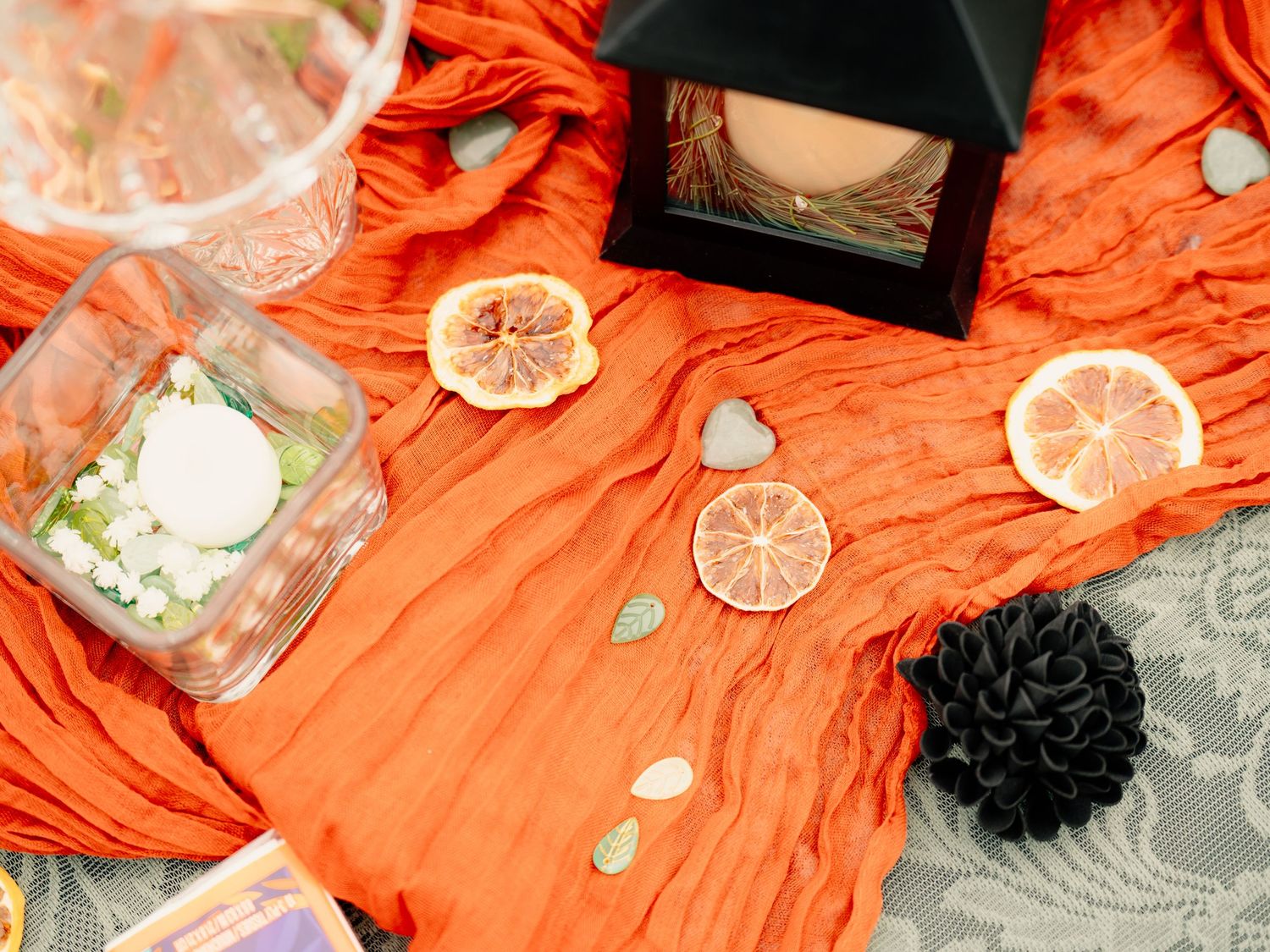 Orange and black decorative Halloween-themed party setup with scattered seashells and paper flowers on a table.