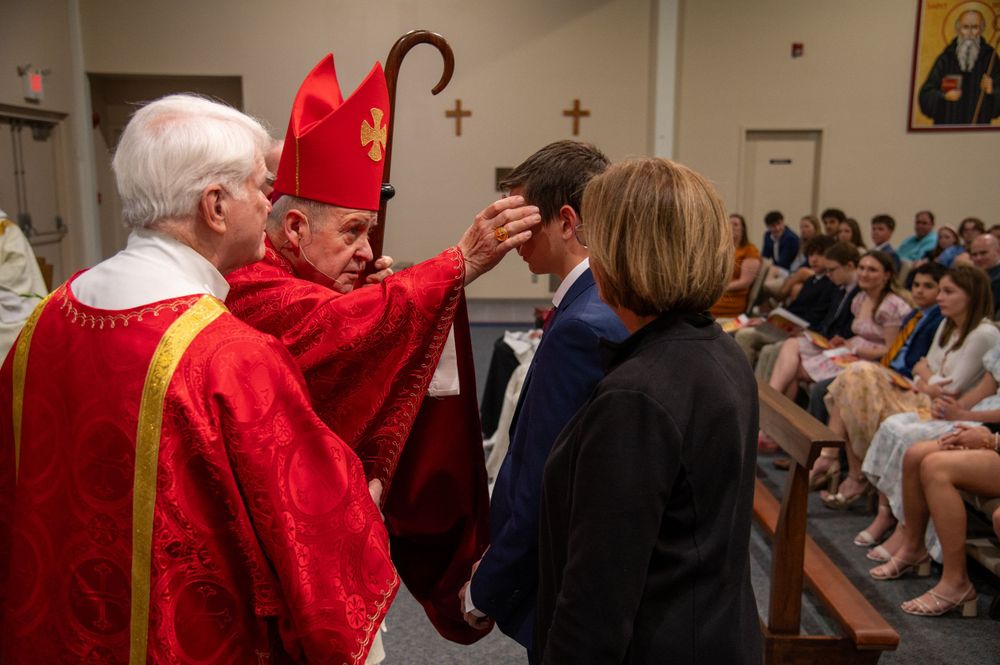 A Bishop anoints the forehead of a Confirmandi with sacred chrism as he confirms him into the Catholic Church.